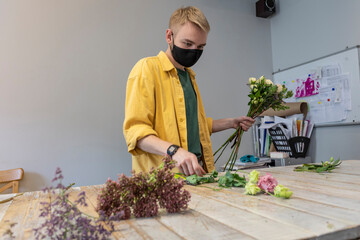 A male florist decorates a flower bouquet in a flower salon.