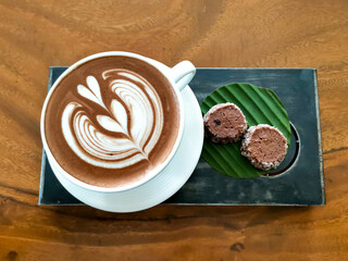 Coffee cup with beautiful latte art and cookies served on a metal plate on a wooden table top.