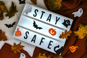 Stay safe. Text in white light box, with a background of sweater, dried leaves halloween autumn...