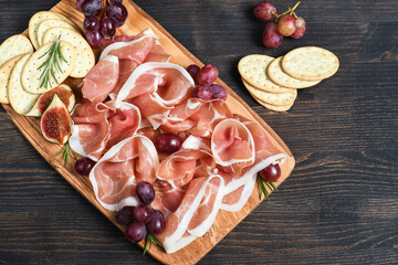 Italian bacon prosciutto crudo or spanish jamon with grapes and crackers on wooden plate. Food for  aperitif and dinner lunch in the restaurant. food delivery home 