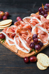 Italian bacon prosciutto crudo or spanish jamon with grapes and crackers on wooden plate. Food for  aperitif and dinner lunch in the restaurant. food delivery home 