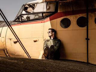 A handsome young pilot sitting on the wing of a plane