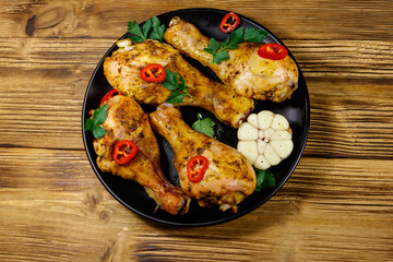 Fototapeta na wymiar Roasted chicken drumsticks with spices in a black plate on a wooden table. Top view