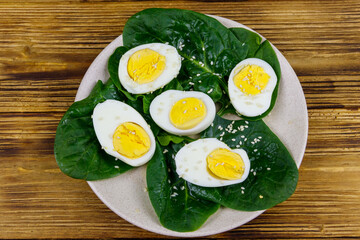 Boiled eggs with fresh spinach leaves and sesame seeds on wooden table. Top view