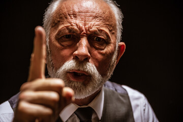 Portrait of angry senior man who threatens. Black background.