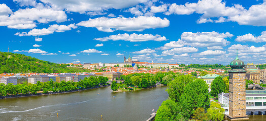 Fototapeta na wymiar Panorama of Prague city historical centre with Prague Castle, St. Vitus Cathedral, Hradcany district, green hills and Vltava river, blue sky. Aerial panoramic view of Prague city, Czech Republic
