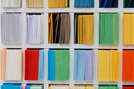 Envelopes stacks sorted on a shelf by color. Colorful mail wraps arranged in categories. Large amount.