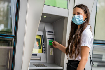 Fototapeta na wymiar Businesswoman with protective mask is using ATM machine to withdraw cash. Covid-19 virus pandemic concept.
