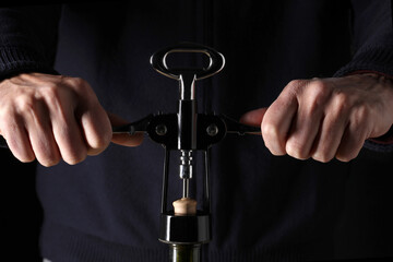 close up on two man's hands opening a wine bottle with opener on black background
