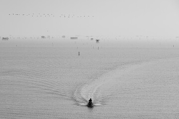 A black and white photo in the morning atmosphere with a boat sailing in the middle of the sea.