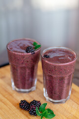 Delicious blackberry smoothie with mint and fresh berries in glasses on wood desk and grey background. Healthy lifestyle concept