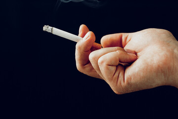 Male hand with a burning cigarette against black background
