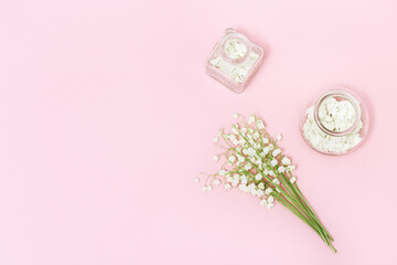 Small flowers of lilies of the valley and glass bottle with dry petals on soft pink background with...