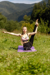 Naklejka na ściany i meble Fitness woman sitting in a yoga pose in a park. Woman practising yoga sitting in a park with palms joined together. lifts the leg up. yoga and stretching, extending leg up, vertical twine