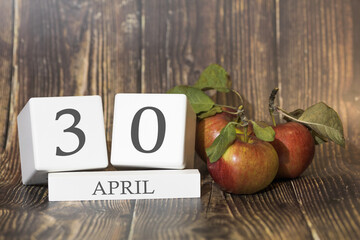 April 30. Day 30 of month. Calendar cube on wooden background with red apples, concept of business and an important event. Spring season.