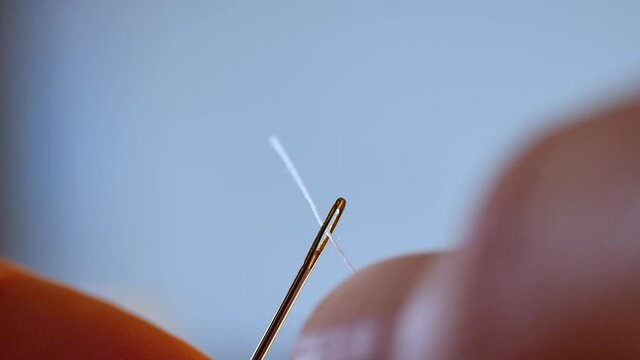 slow motion shot of white thread passing through sewing needle. man sewing project by hand. handmade fashion with quality thread and fabric. DIY and beautiful quilting by fashion designer. embroidery 