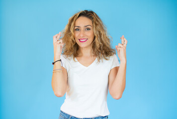 Fototapeta premium Beautiful woman with curly hair wearing white casual t-shirt over isolated background gesturing finger crossed smiling with hope. Luck and superstitious concept.