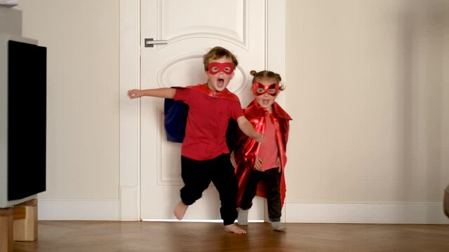 Cute little children wearing stylish superheroes costumes run to camera from white door in spacious light room at party