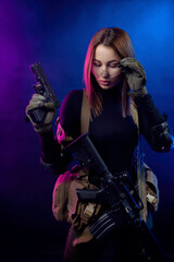 Obraz na płótnie Canvas a woman in military airsoft uniform with an American automatic rifle and pistol on a dark background