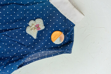 Flat lay of polka dot blouse and brooch on white concrete background. The brooch is made of beads,...