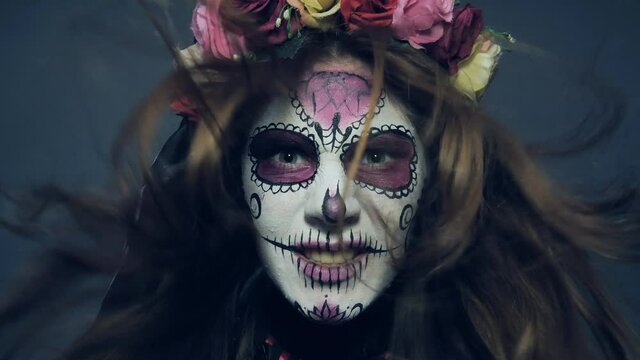 Halloween makeup, Santa Muerte or sugar Mexican skull, makeup. The girl screams and laughs with developing hair. Slow motion