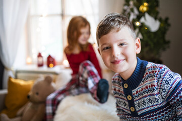 Small girl and boy in pajamas indoors at home at Christmas, playing.