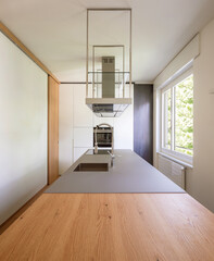 Modern kitchen with suspended hood, large sink, oven and wooden worktop. Frontal view