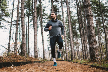 Young smiling sportswoman with healthy habits running in woods at autumn and preparing for marathon.