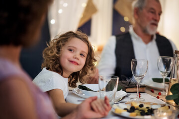 Small girl with grandparents sitting indoors celebrating Christmas together.