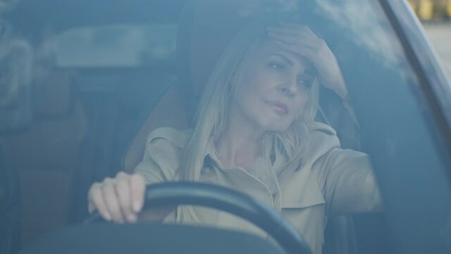 The stressed woman driver is sitting inside her car. Sad business woman is having headache has to make a stop after driving car in traffic jam on rush hour. Exhausted, overworked driver concept.