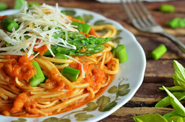 Spaghetti pasta in tomato sauce with asparagus sprinkled with grated Parmesan cheese on a wooden background