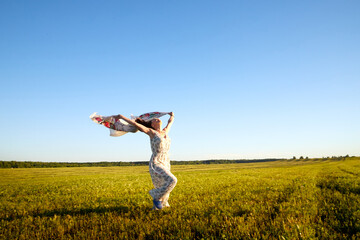 Fototapeta premium Beautiful woman or girl with magnificent figure and plastic movements walking and dancing in green field with trimmed grass in the setting sun during sunset with warm yellow light.