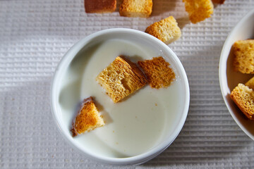 Square toasted pieces of homemade delicious rusk, hardtack, Dryasdust, zwieback and plate of milk on a white tablecloth.