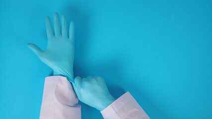 Doctor's hand is pulling blue latex gloves on blue background.