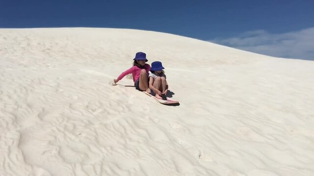 Two young girls having fun sliding down Lancelin sand dunes near Lancelin Western Australia