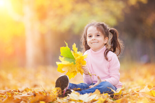 Happy girl playing yellow leaves in the autumn park. Beauty nature scene with family outdoor lifestyle. Happy girl having fun outdoor. Happiness and harmony in childhood