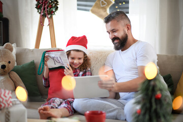 Father with small daughter indoors at home at Christmas, using tablet.