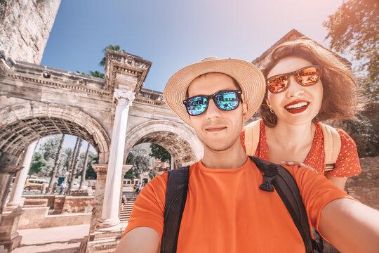 A man and a woman in love embrace and take a selfie photo against the backdrop of the archaeological ruins of Hadrian's gate in Antalya. Honeymoon in Turkey concept