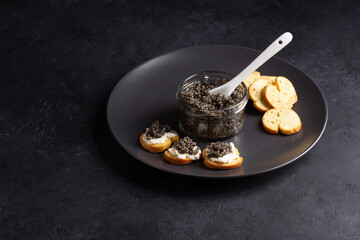Sandwiches with black caviar on black background. Sturgeon caviar in glass can. Copy space.