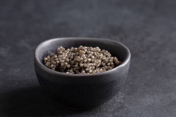 Sturgeon black caviar in black bowl on black background. Copy space. Close-up.