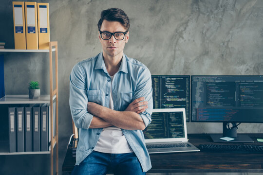 Portrait of confident expert smart guy it manager cross hands work distance ready solve cyber space java script errors bug sit desk wear denim jeans shirt in workplace workstation