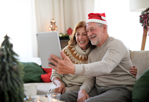 Side view of senior couple indoors at home at Christmas, having video call with family.