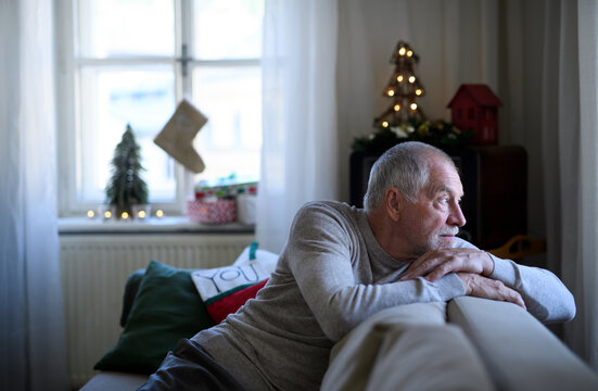 Lonely senior man sitting on sofa indoors at Christmas, solitude concept.