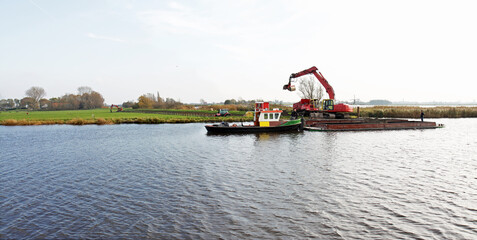 A push boat with a barge of clay being unloaded for dike improvement works, in a traditional Dutch polder landscape.