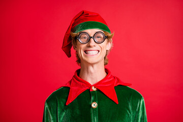 Portrait of christmas fairy funky elf guy in geek style specs toothy smiling in camera isolated on red color background