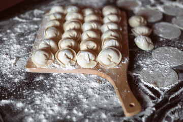 homemade dumplings lie on a wooden cutting board on the kitchen table. Image with selective focus and noise effect