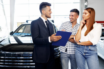 Obraz premium Man car salesman telling about the features of the new car to the couple