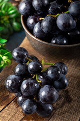 Fresh black grapes and leaves on a rustic timber on dark stone background.