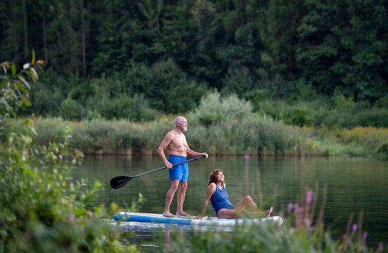 Senior Couple Paddleboarding On Lake In Summer.