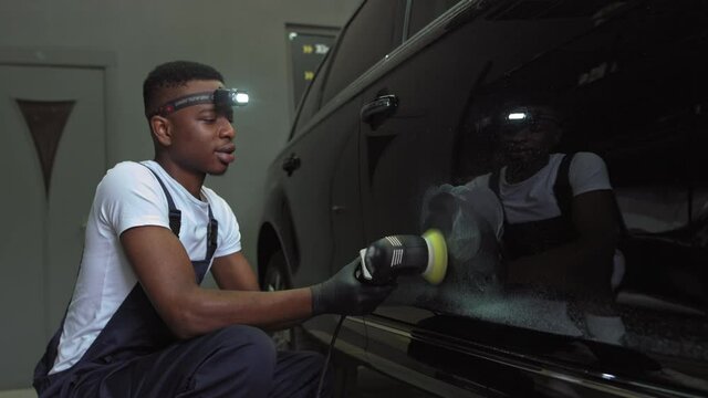 A young African-American polishes a car.Car detailing - Men are using machinery car polishers maintenance to remove marks repair according to the surface of the car's paint before continuing to coat